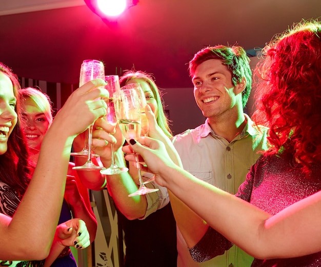 concetto di festa, vacanze, celebrazione, vita notturna e persone - amici sorridenti che tintinnano bicchieri di champagne nel club