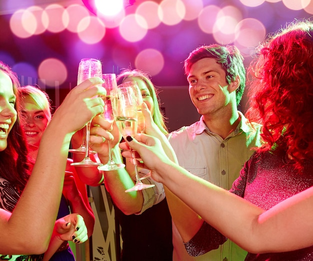 concetto di festa, vacanze, celebrazione, vita notturna e persone - amici sorridenti che tintinnano bicchieri di champagne nel club