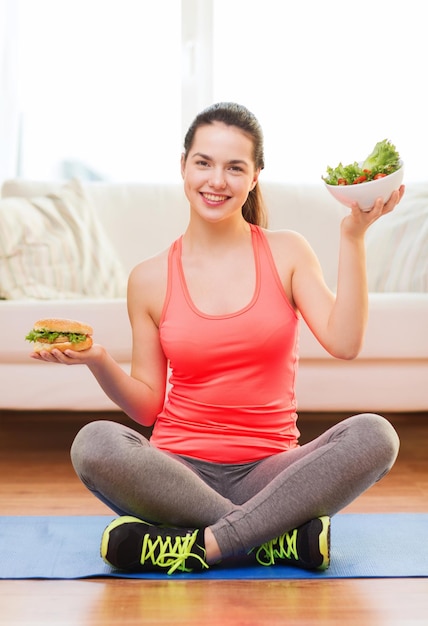 concetto di fitness, casa e dieta - adolescente sorridente con insalata verde e hamburger a casa