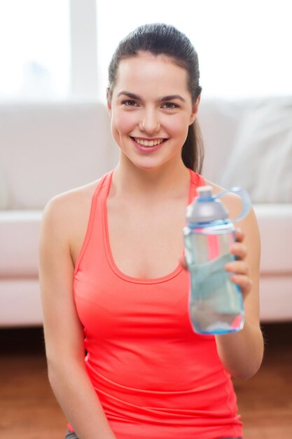 concetto di fitness, casa e dieta - adolescente sorridente con una bottiglia d'acqua dopo l'esercizio a casa