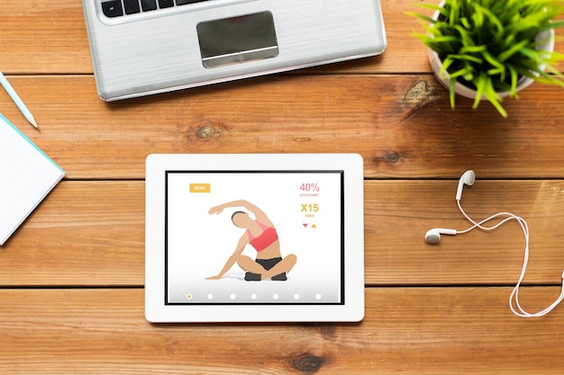 concetto di fitness e tecnologia - primo piano del computer tablet pc, laptop e auricolari sul tavolo di legno con applicazione sportiva sullo schermo