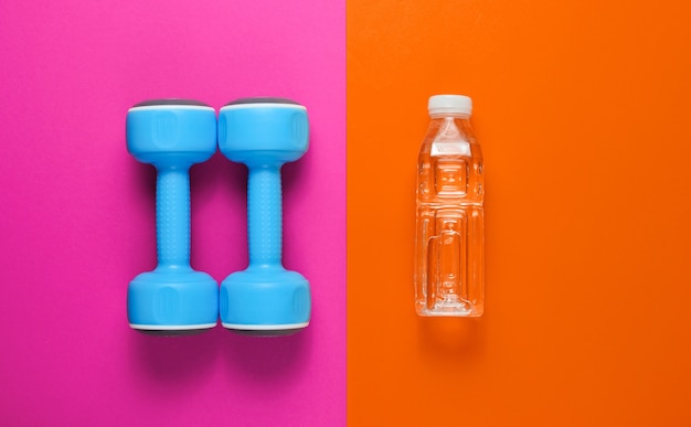 Concetto di fitness minimalista. Manubri, bottiglia d'acqua colorata