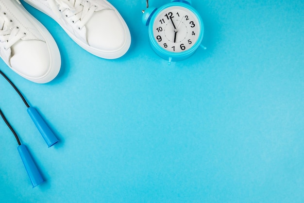 Concetto di fitness È ora di fare sport Foto vista dall'alto di sneaker bianche sveglia e corda per saltare su sfondo blu isolato con spazio per la copia