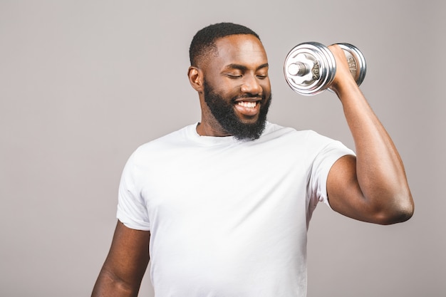 Concetto di fitness. Ritratto di un uomo di colore afroamericano felice con le teste di legno isolate sopra fondo grigio.