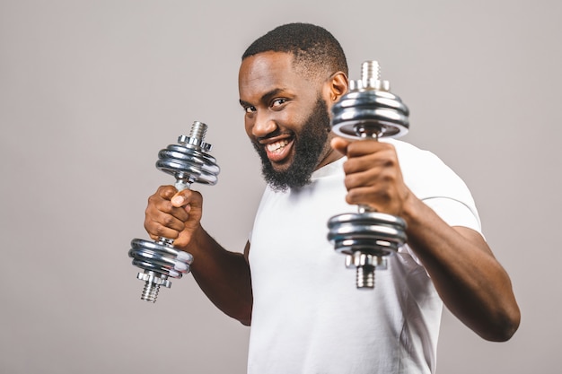 Concetto di fitness. Ritratto di un uomo di colore afroamericano felice con le teste di legno isolate sopra fondo grigio.