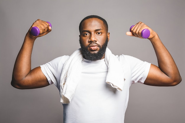 Concetto di fitness. Ritratto di un uomo di colore afroamericano felice con le teste di legno isolate sopra fondo grigio.