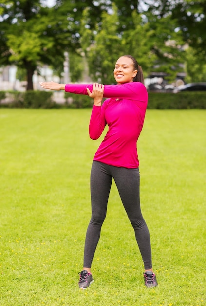 concetto di fitness, sport, allenamento, parco e stile di vita - donna sorridente che allunga la gamba all'aperto