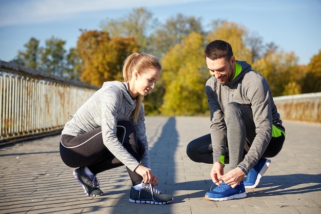 concetto di fitness, sport, allenamento, persone e stile di vita - coppia sorridente che lega i lacci delle scarpe da ginnastica all'aperto