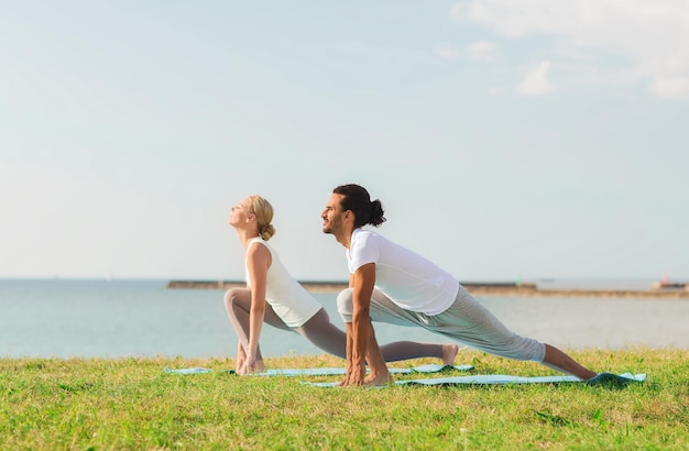 concetto di fitness, sport, amicizia e stile di vita - coppia sorridente che fa esercizi di yoga su stuoie all'aperto