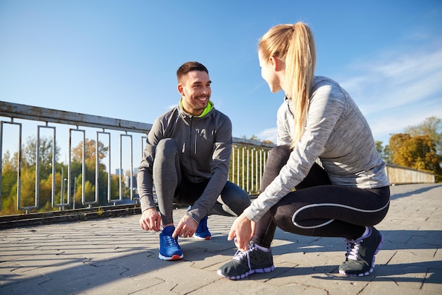 concetto di fitness, sport, amicizia e stile di vita - coppia sorridente che lega i lacci delle scarpe all'aperto