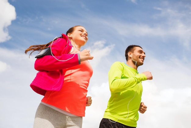 concetto di fitness, sport, amicizia e stile di vita - coppia sorridente con auricolari in esecuzione all'aperto