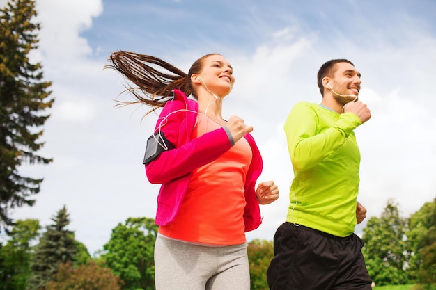 concetto di fitness, sport, amicizia e stile di vita - coppia sorridente con auricolari in esecuzione all'aperto