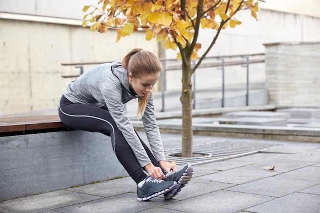 concetto di fitness, sport, amicizia e stile di vita - felice giovane donna sportiva che lega i lacci delle scarpe all'aperto