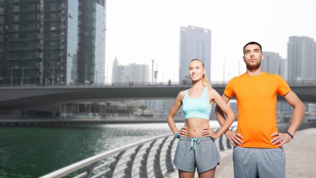 concetto di fitness, sport e stile di vita sano - coppia sorridente che si esercita sulla strada della città di dubai e sullo sfondo della riva