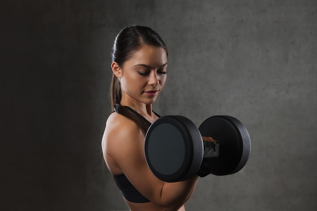 concetto di fitness, sport, esercizio, allenamento e persone - giovane donna che flette i muscoli con i manubri in palestra