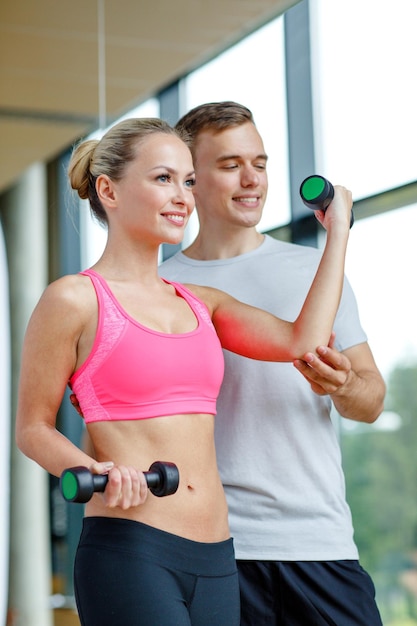 concetto di fitness, sport, esercizio e dieta - giovane donna sorridente e personal trainer con manubri in palestra