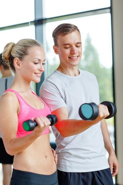 concetto di fitness, sport, esercizio e dieta - giovane donna sorridente e personal trainer con manubri in palestra