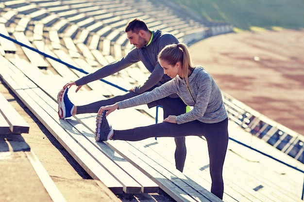 concetto di fitness, sport, esercizio fisico e stile di vita - coppia che allunga la gamba sugli spalti dello stadio