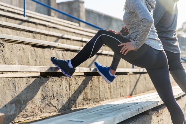 concetto di fitness, sport, esercizio fisico e stile di vita - primo piano di una coppia che allunga la gamba sugli spalti dello stadio