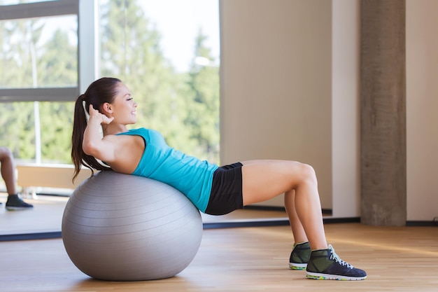 concetto di fitness, sport, formazione e persone - donna sorridente che flette i muscoli addominali con palla ginnica in palestra