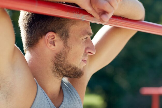 concetto di fitness, sport, formazione e stile di vita - giovane che si esercita sulla barra orizzontale all'aperto