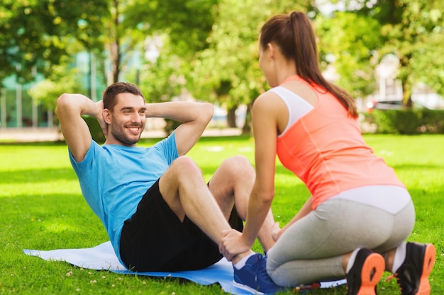 concetto di fitness, sport, formazione, lavoro di squadra e stile di vita - uomo sorridente con personal trainer che fa esercizi sul tappetino all'aperto