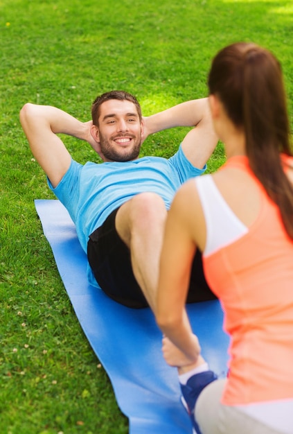 concetto di fitness, sport, formazione, lavoro di squadra e stile di vita - uomo sorridente con personal trainer che fa esercizi sul tappetino all'aperto