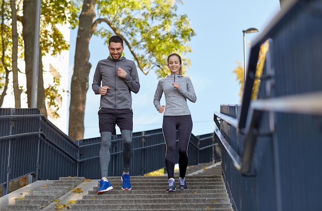 concetto di fitness, sport, persone e stile di vita - coppia felice che corre al piano di sotto in città