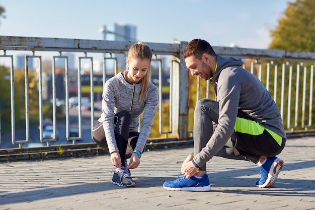 concetto di fitness, sport, persone e stile di vita - coppia sorridente che lega i lacci delle scarpe all'aperto