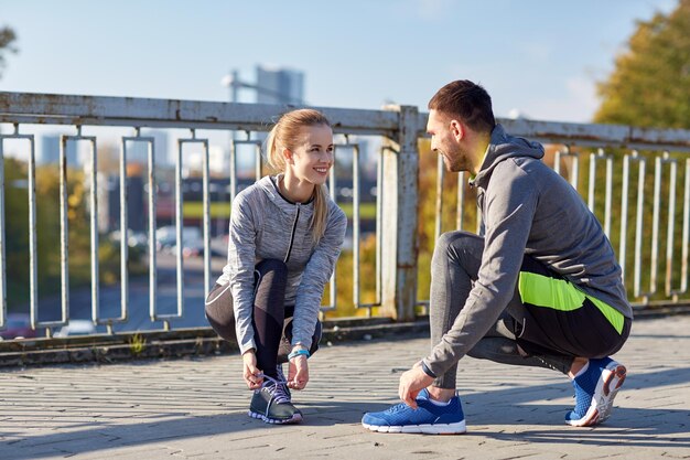 concetto di fitness, sport, persone e stile di vita - coppia sorridente che lega i lacci delle scarpe all'aperto