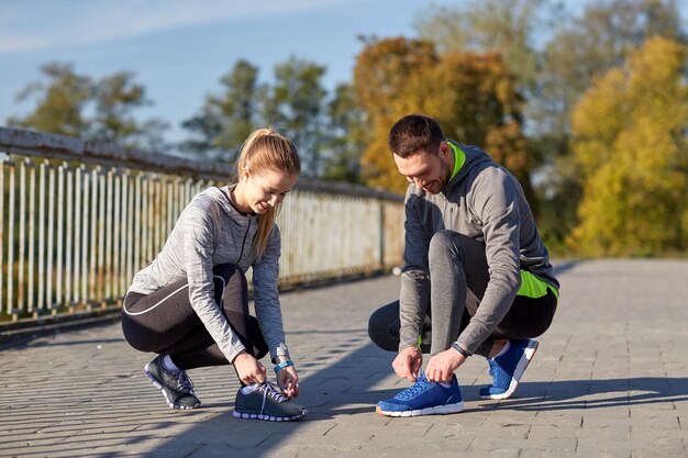 concetto di fitness, sport, persone e stile di vita - coppia sorridente che lega i lacci delle scarpe all'aperto