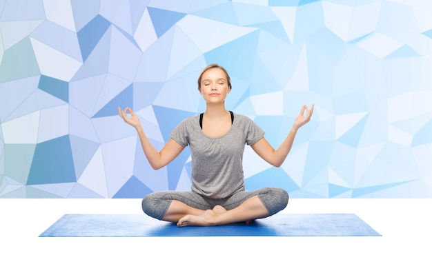 concetto di fitness, sport, persone e stile di vita sano - donna che fa meditazione yoga nella posa del loto sul tappeto su sfondo basso poli