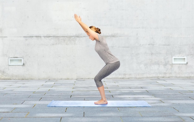 concetto di fitness, sport, persone e stile di vita sano - donna che fa yoga in sedia posa su tappetino su sfondo strada urbana