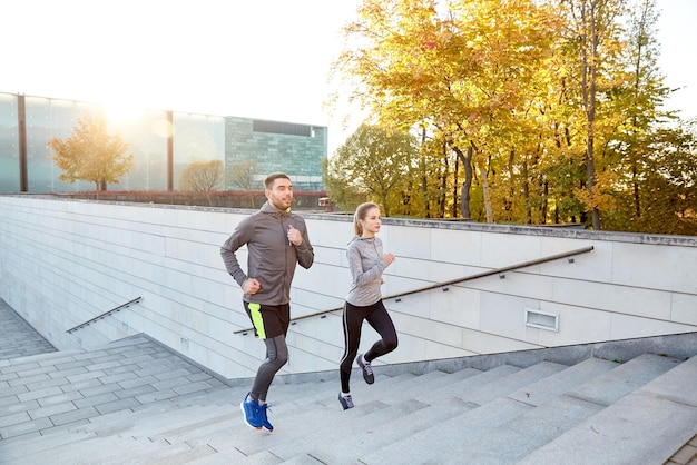 concetto di fitness, sport, persone, esercizio e stile di vita - coppia felice che corre al piano di sopra sulle scale della città