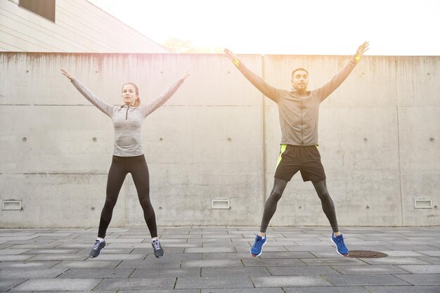 concetto di fitness, sport, persone, esercizio fisico e stile di vita - uomo e donna felici che fanno esercizi di salto con jack o stelle all'aperto