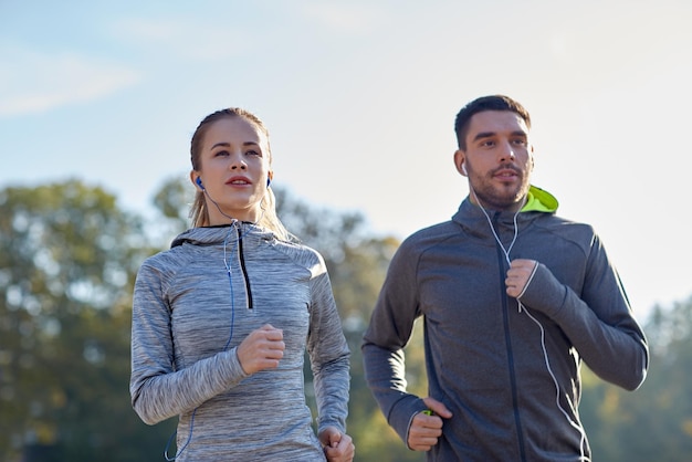 concetto di fitness, sport, persone, tecnologia e stile di vita - coppia felice che corre e ascolta musica in auricolari all'aperto