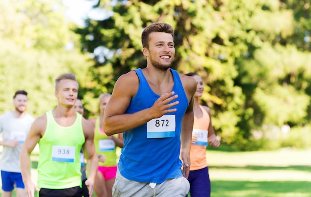 concetto di fitness, sport, razza e stile di vita sano - gruppo di amici adolescenti felici o sportivi che corrono maratona con numeri di badge all'aperto