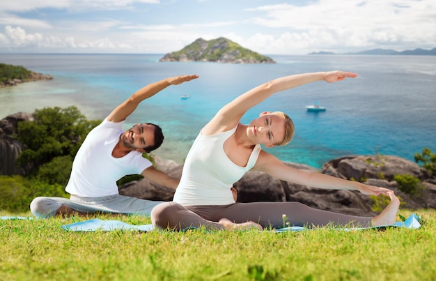 concetto di fitness, sport, relax e persone - coppia felice che fa esercizi di yoga seduti su stuoie all'aperto su sfondo naturale