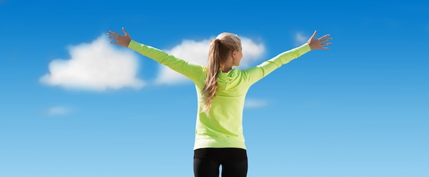 concetto di fitness, sport, successo, persone ed emozioni - donna sportiva felice che gode del sole e della libertà su sfondo blu cielo e nuvole dal retro