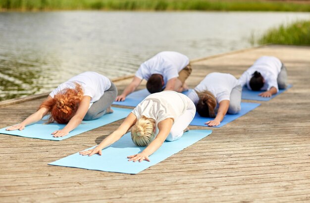 concetto di fitness, sport, yoga e stile di vita sano - gruppo di persone che fanno la posa dei bambini sull'ormeggio del fiume o del lago
