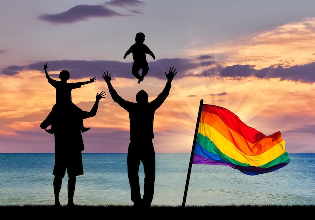 Concetto di genitori gay. Silhouette di genitori gay felici con bambini sullo sfondo del tramonto sul mare e una bandiera arcobaleno