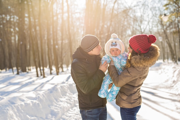 Concetto di genitorialità, moda, stagione e persone - famiglia felice con bambino in abiti invernali all'aperto.