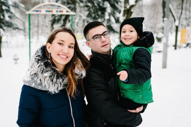 Concetto di genitorialità, moda, stagione e persone - famiglia felice con bambino in abiti invernali che cammina all'aperto nel parco.