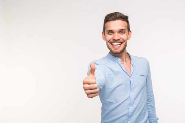 Concetto di gesto e persone - uomo bello con un sorriso che mostra il pollice in su sul muro bianco con spazio di copia.