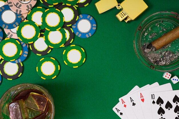 Concetto di gioco d'azzardo, fortuna e intrattenimento - primo piano di fiches del casinò, bicchiere di whisky, carte da gioco e sigaro sulla superficie del tavolo verde. Vista dall'alto. Natura morta