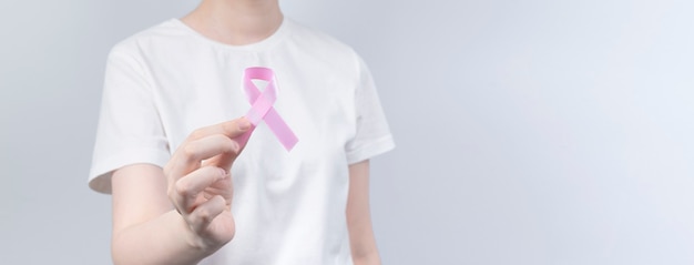 Concetto di giornata mondiale del cancro al seno. La donna in maglietta bianca tiene il nastro rosa in mano. Ottobre mese della consapevolezza del cancro al seno.