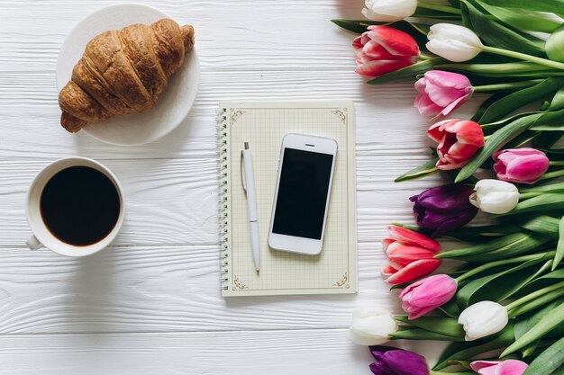 Concetto di giorno della madre Bouquet di tulipani, caffè, croissant e smartphone.