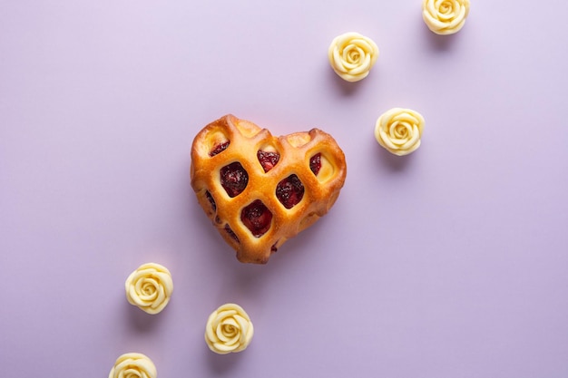 Concetto di giorno di San Valentino Panino a forma di cuore con crosta reticolare e marmellata di bacche su uno sfondo lilla con rose di cioccolato bianco Spazio di copia piatto