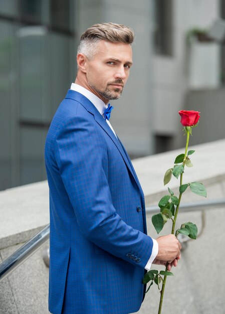 Concetto di giorno di San Valentino uomo smoking canuto con regalo di fiori di rosa di San Valentino per San Valentino