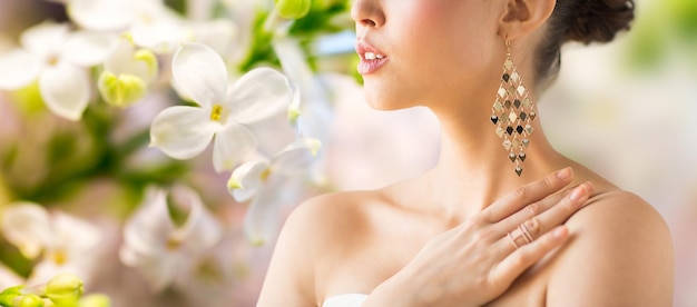 concetto di glamour, bellezza, gioielleria e lusso - primo piano di bella donna con orecchini su sfondo di fiori lilla primaverili naturali